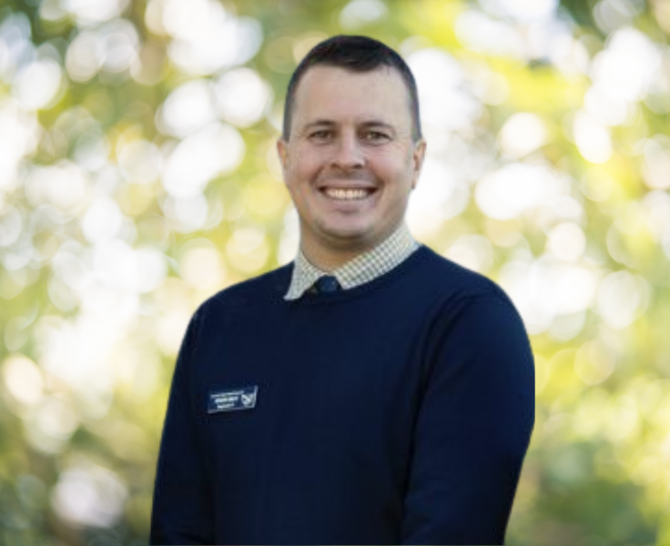 Head shot photo of Mr Irwin smiling in front of a nature background.
