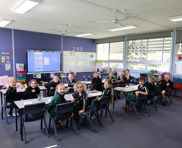 A classroom with students looking over the shoulders at the camera smiling.