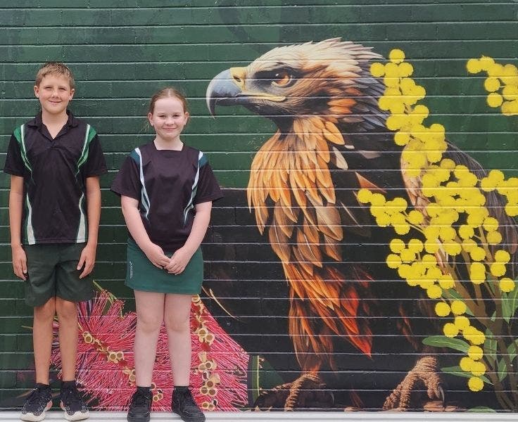 Students in school uniform standing in front of a mural.