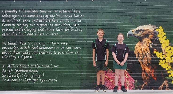 Two students standing in front of a mural with an Acknowledgement of Country and eagle on them.